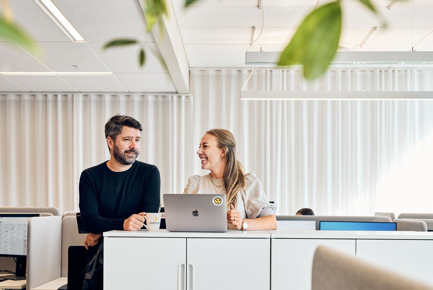 Two colleagues leaning against a desk chatting with each other