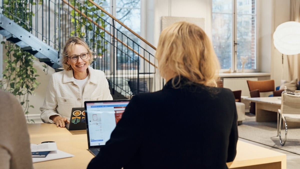 Two female colleagues sitting by their desks chatting while working