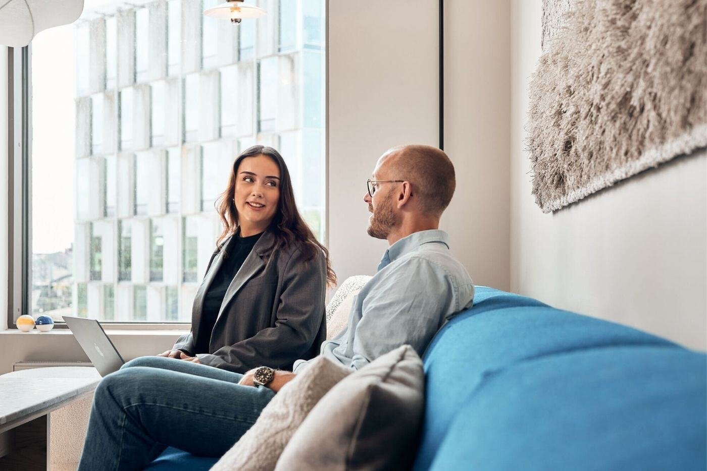 A female and a male colleague sitting in the lounge area conversing 
