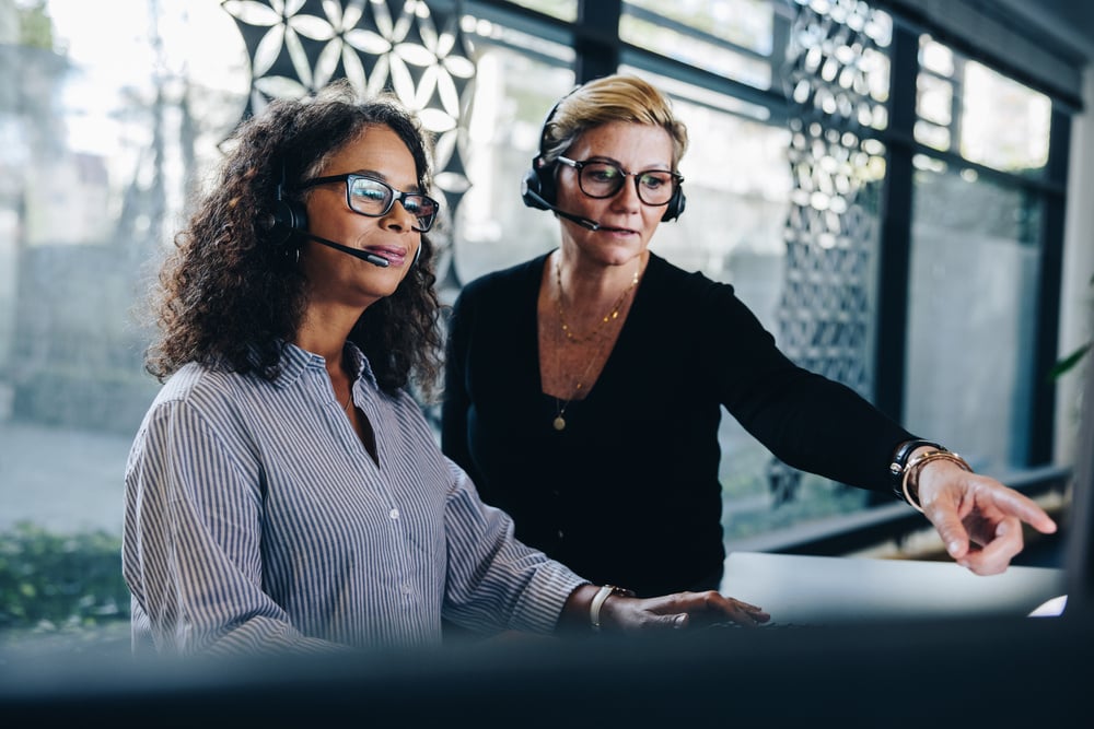 Two women wearing headsets looking at a computer screen