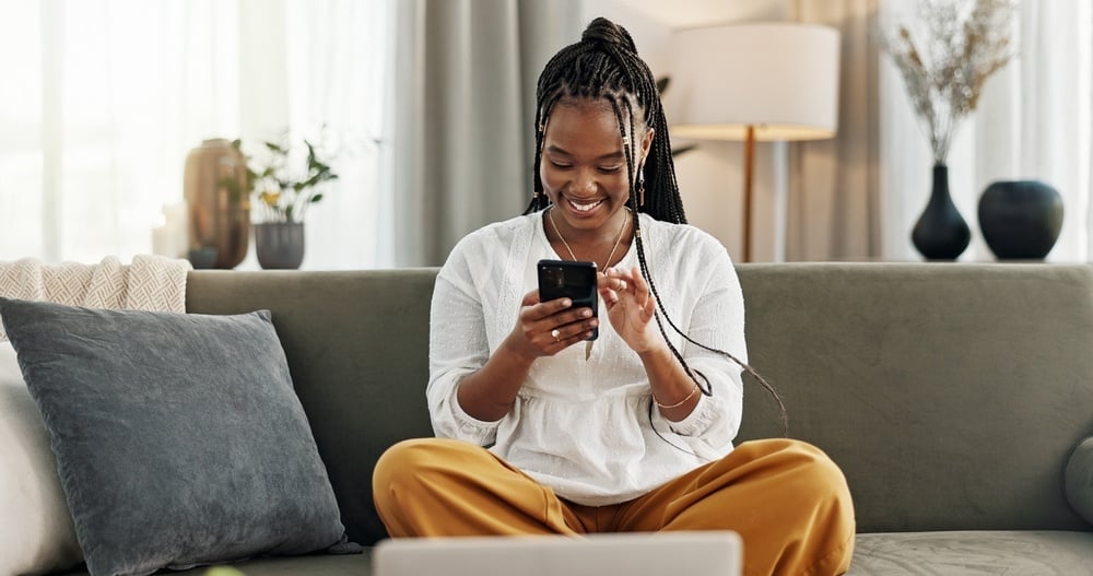 Young girl sitting in a sofa scrolling on her mobile while smiling